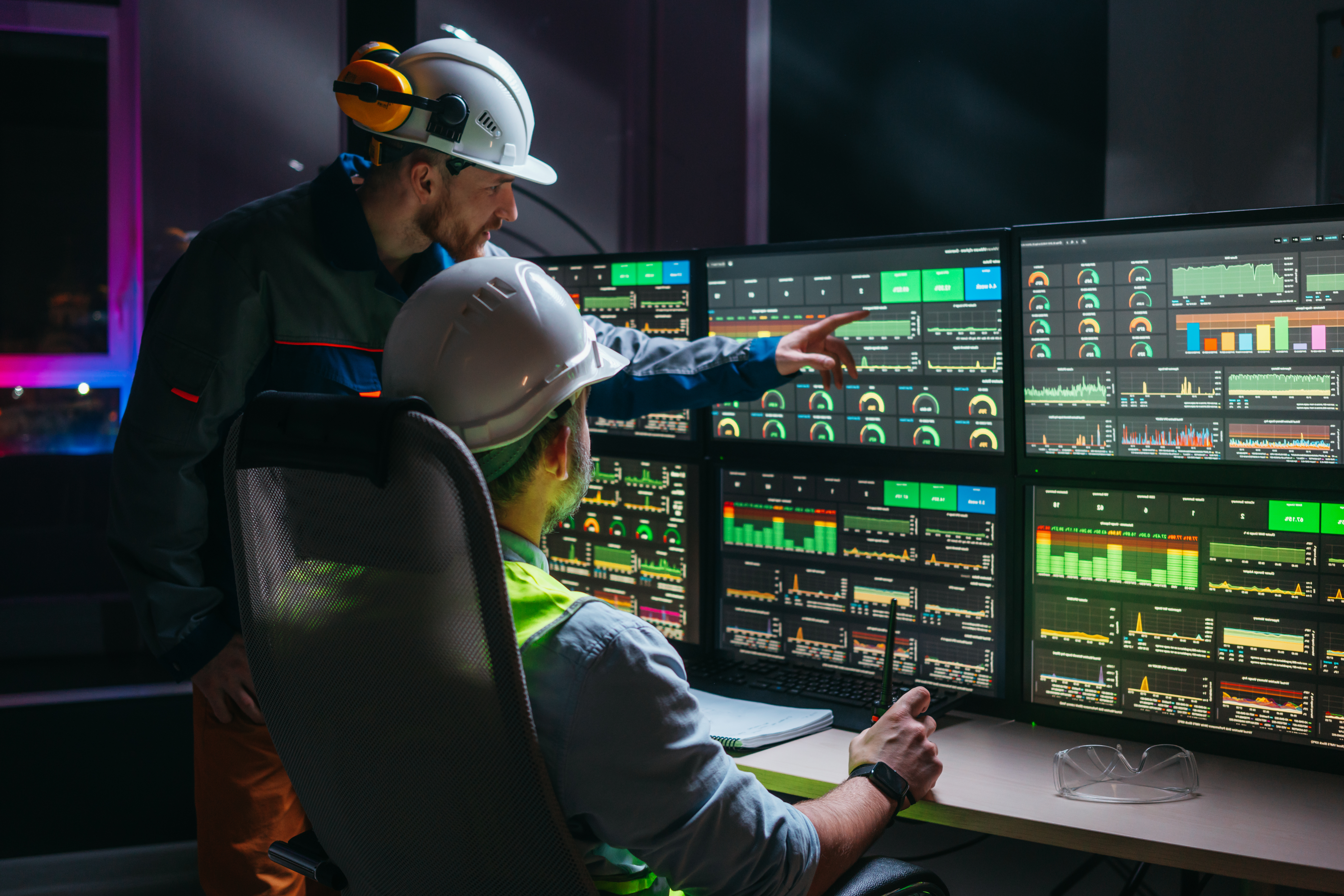 Head engineer and factory operator wearing safety vests and hard hats wollowing product process on factory uses SCADA system and industry 4.0. Two operators controll assembly line using screens with human-machine interface